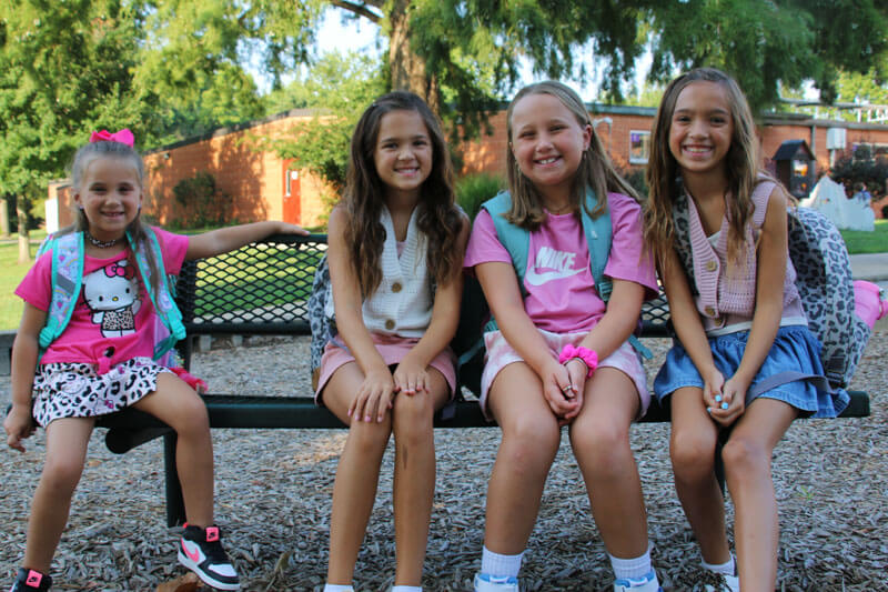 Four Bowles students smile together on the school playground